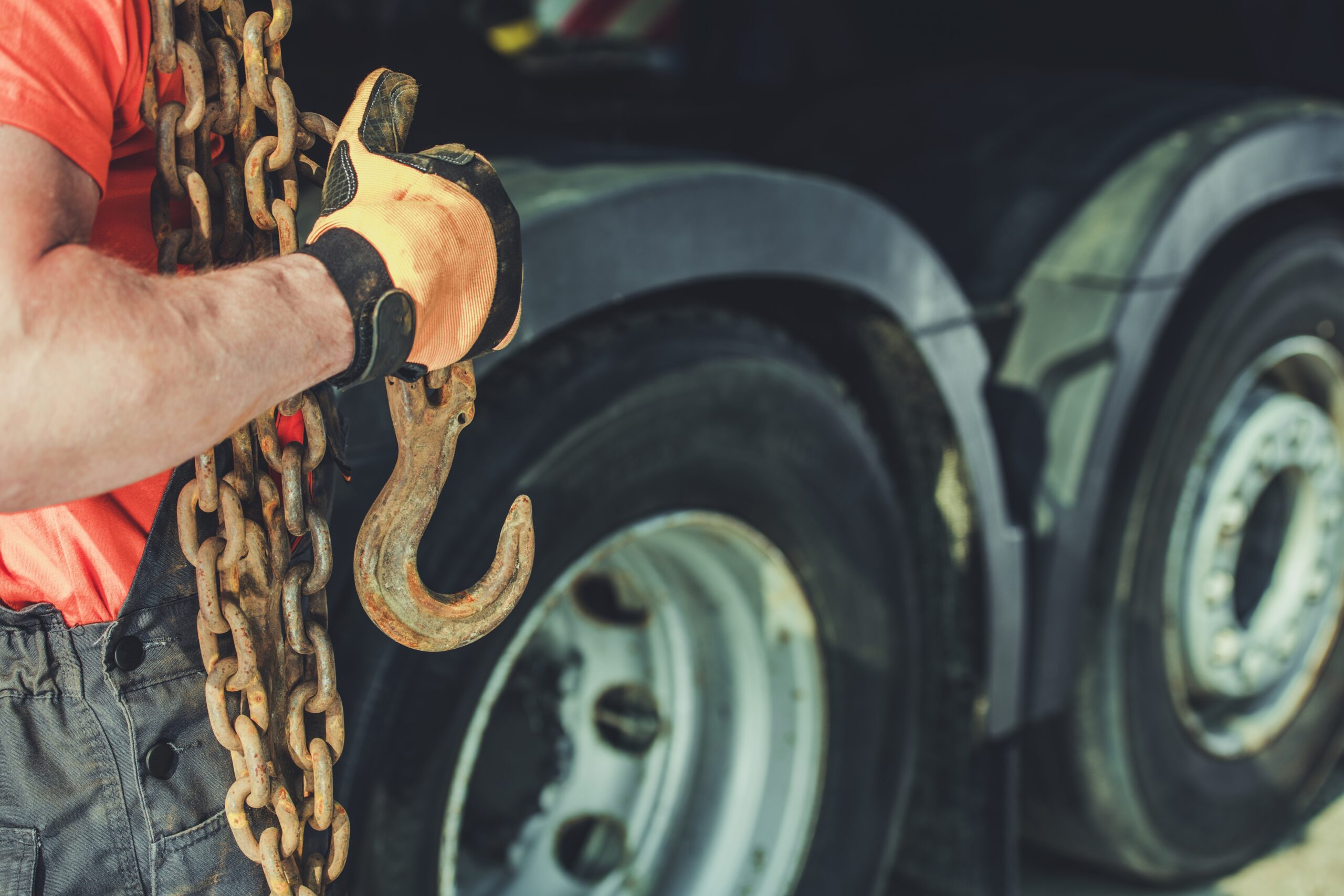 A worker holds a tow hook in front of a wrecker service Houston truck.